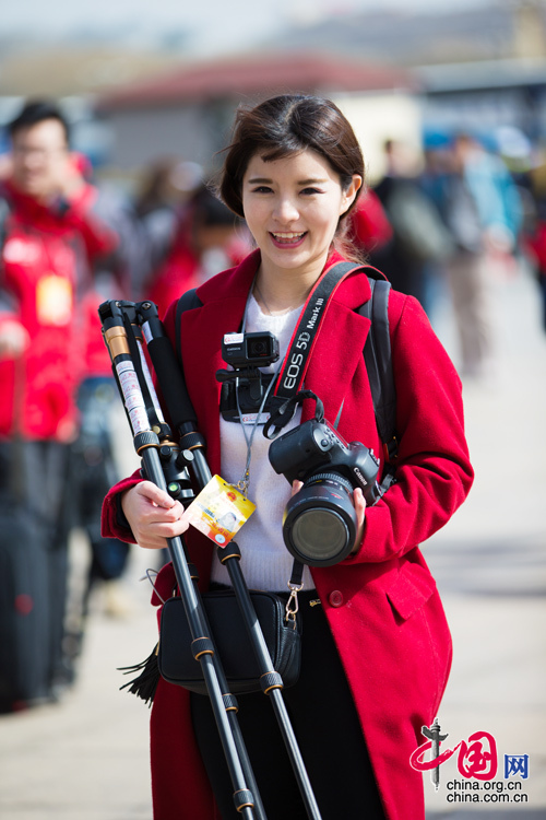 2016年兩會,人民大會大堂前,一位笑容燦爛的紅衣女記者正步入大會堂。中國網 鄭亮 攝